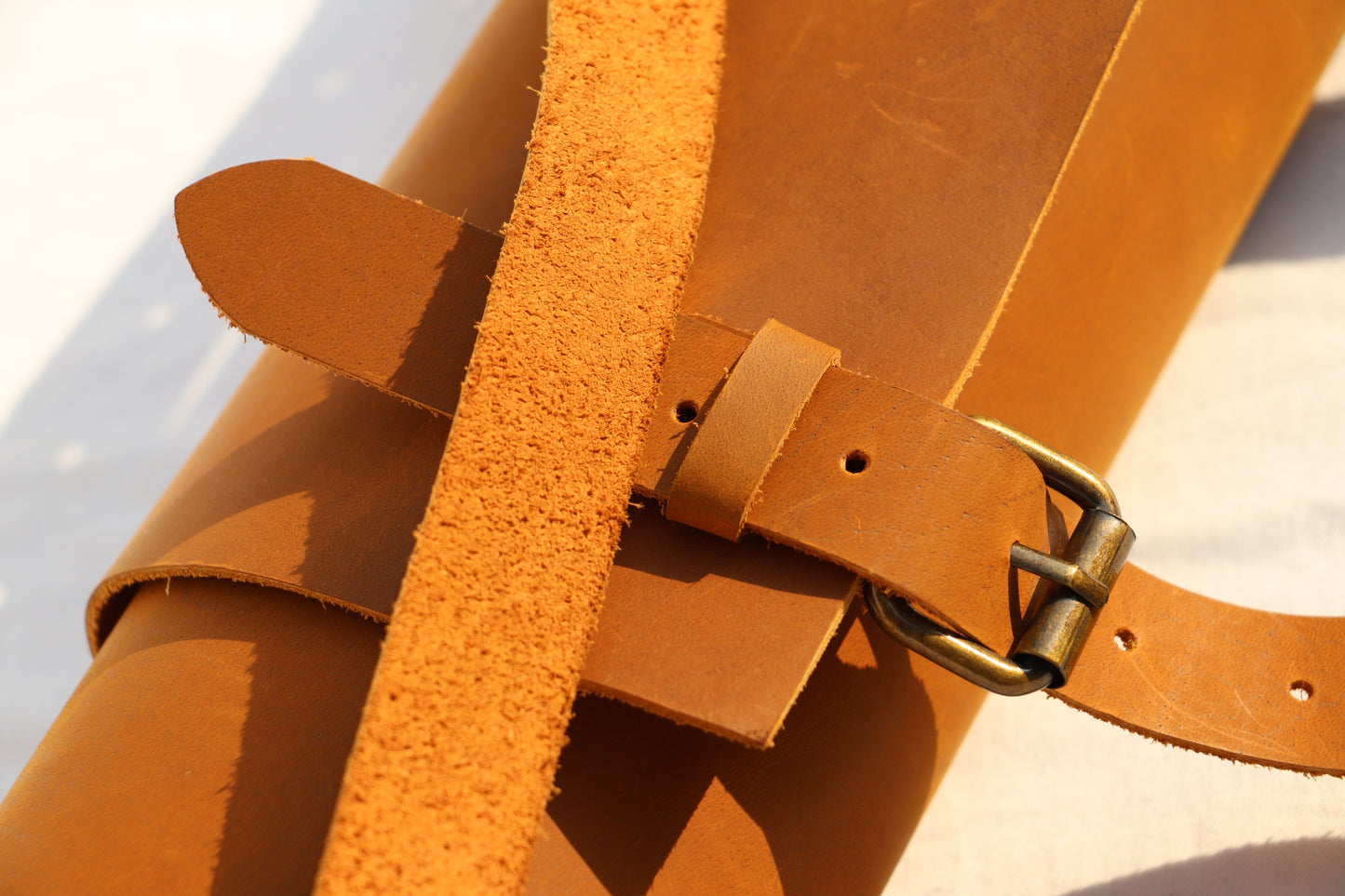 Close-up of a brown leather belt with a brass buckle on a light background