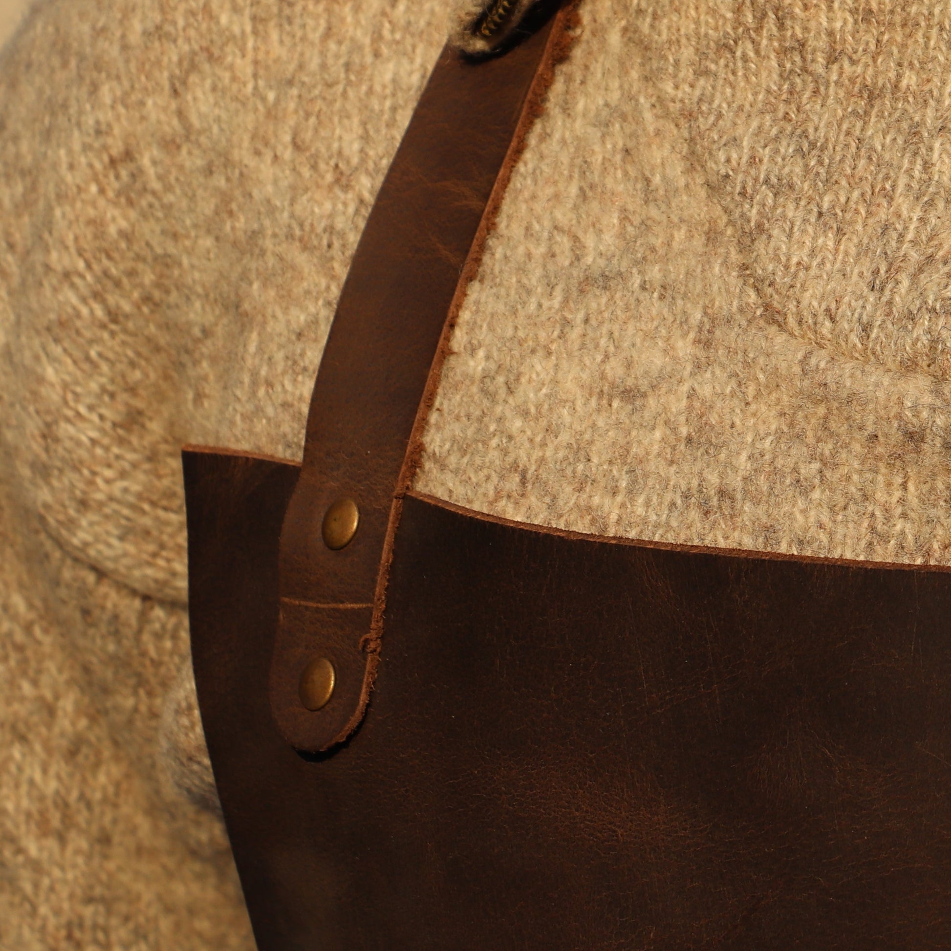 Person wearing a textured sweater with a leather apron over a neutral background