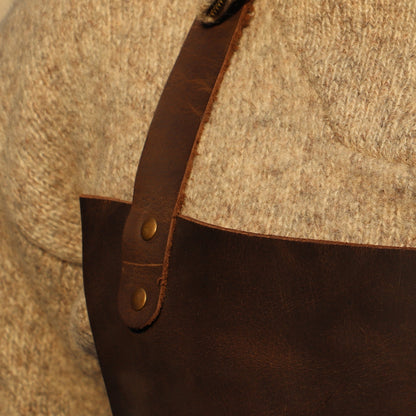 Person wearing a textured sweater with a leather apron over a neutral background